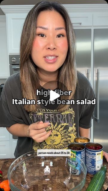 a woman standing in front of a glass bowl filled with vegetables and sauces on top of a kitchen counter