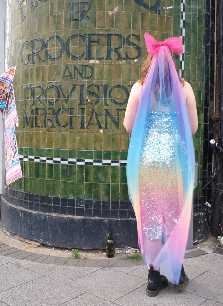 a woman in a colorful dress is standing on the sidewalk with her back to the camera