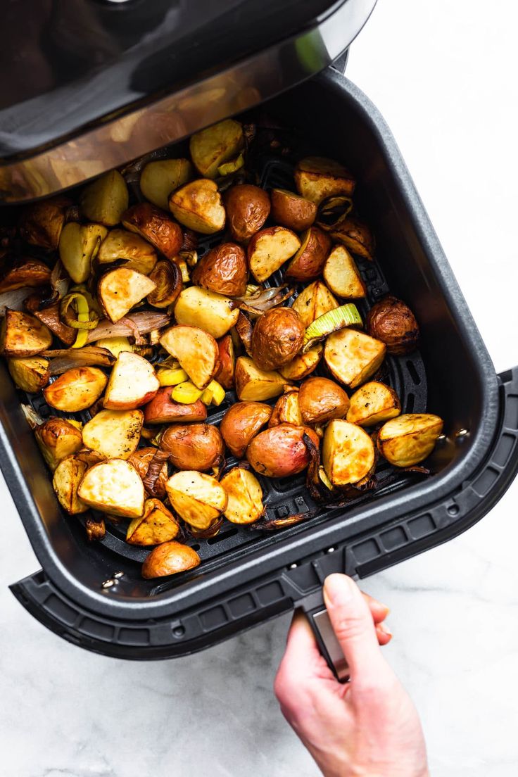 roasted potatoes in an air fryer being held by a person's hand with the lid open