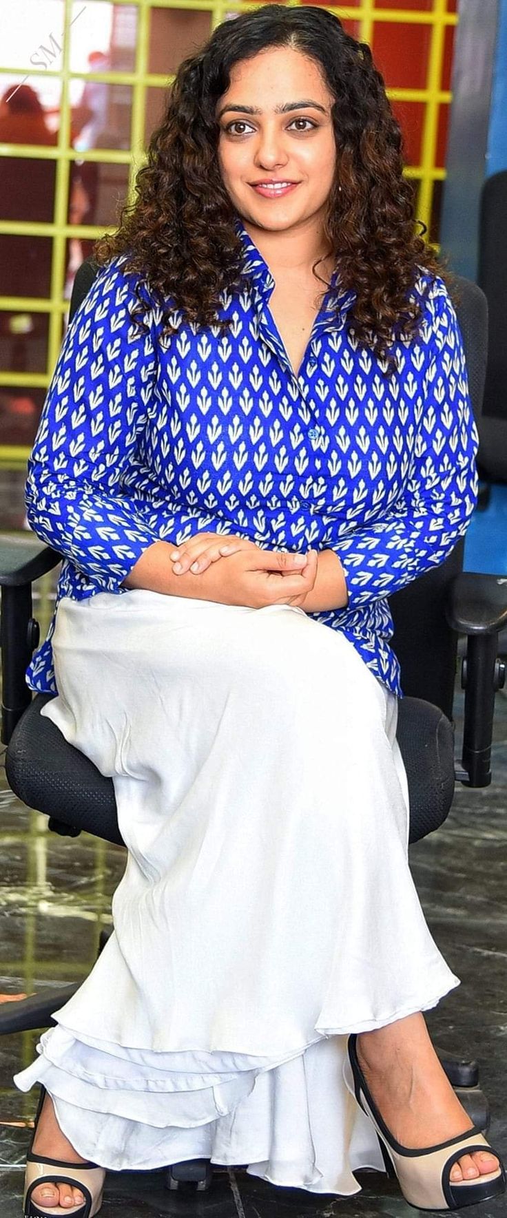 a woman sitting in a chair with her arms crossed and legs crossed, smiling at the camera