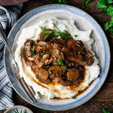 mashed potatoes topped with mushrooms and gravy in a bowl on top of a wooden table