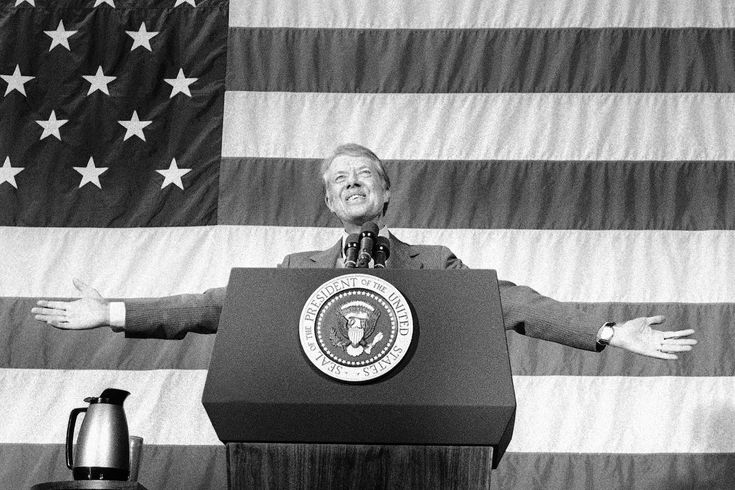 a man standing at a podium with his arms outstretched in front of an american flag