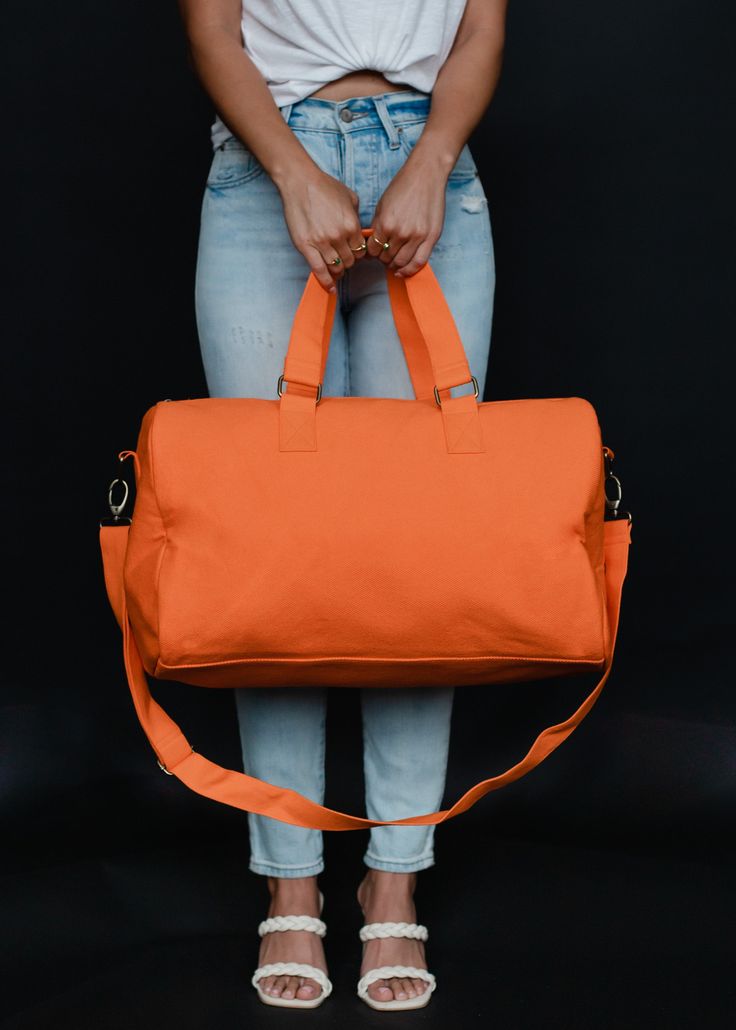 Orange duffel bag Red " getaway" textured text on the front Zipper closure with interior zipper pocket and 2 small open pockets Removable strap Measures 12" x 9" x 19.5" 100% Cotton Lining: 100% Polyester Casual Gym Bag With Pockets For Weekend Trips, Casual Duffle Bag With Zipper Pocket For Weekend Trips, Solid Travel Bag With Zipper Closure, Overnight Duffle Bag With Adjustable Strap, Travel Bag With Zipper Closure, Weekend Tote Duffle Bag With Luggage Sleeve, Casual Tote Duffle Bag With Zipper Closure, Casual Duffle Bag Tote With Zipper Closure, Casual Weekender Bag With Zipper Pocket For Overnight Trips