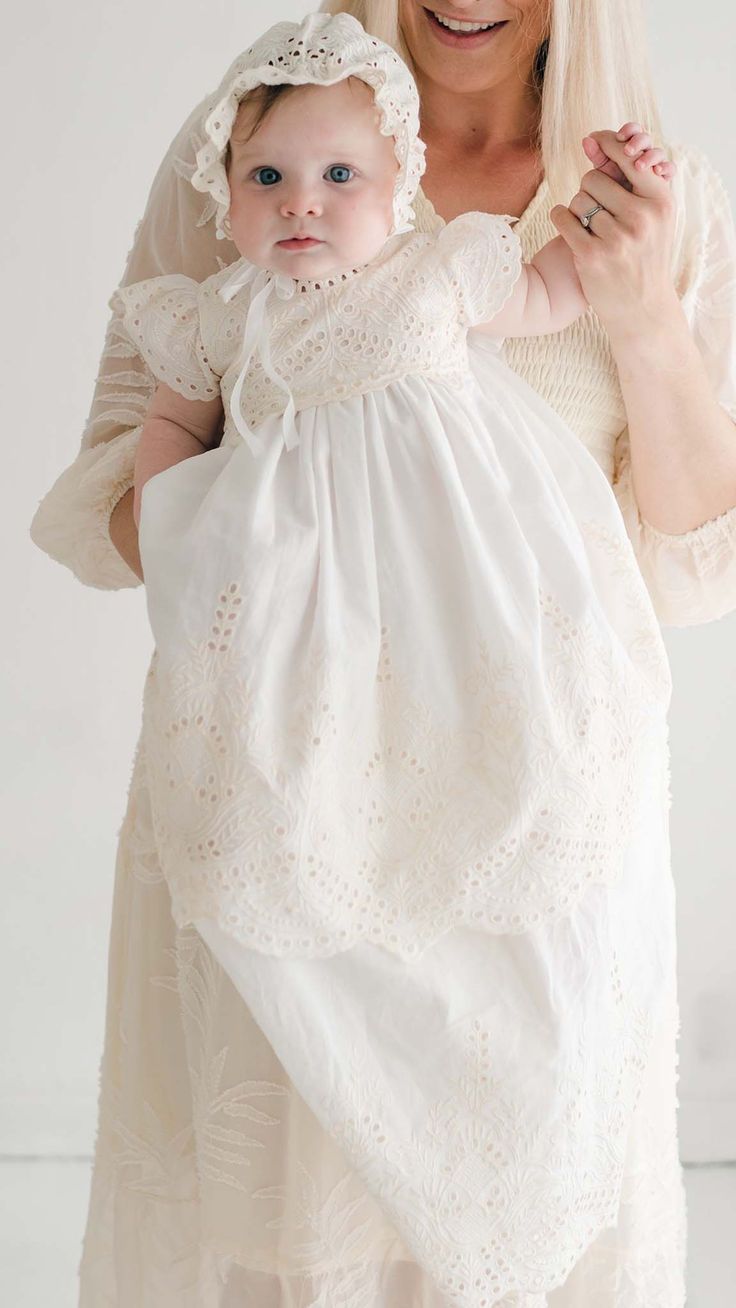 a woman holding a baby wearing a white dress and headband with her hands in the air