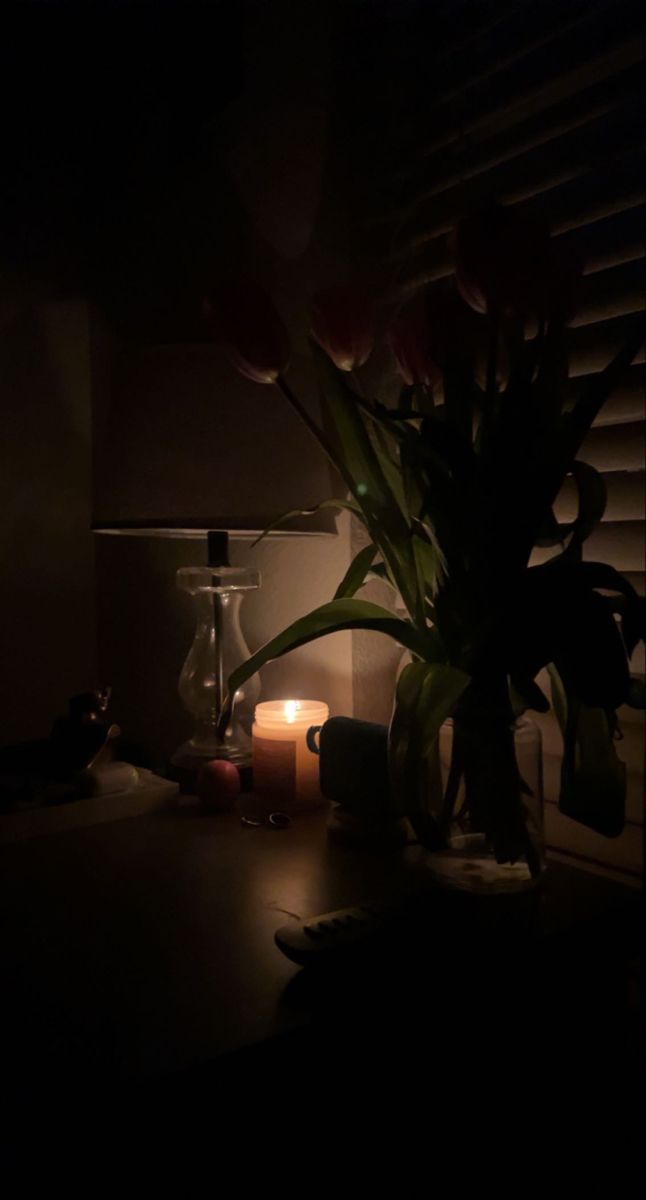 a vase with some flowers in it sitting next to a candle on a table near a window