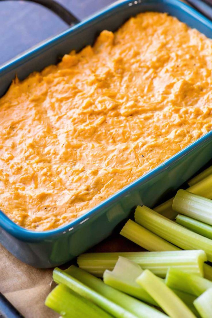 carrot dip in a blue casserole dish with celery and celery stalks