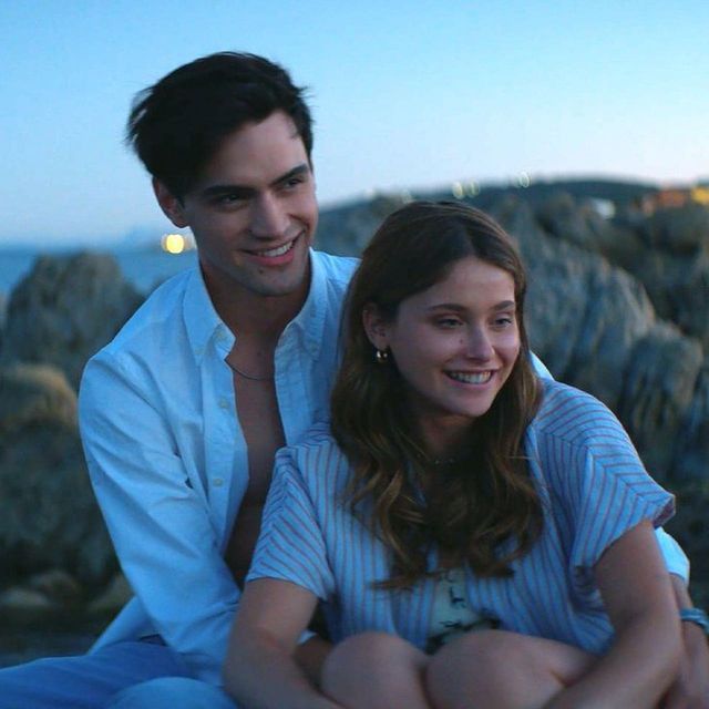 a man sitting next to a woman on top of a rocky cliff near the ocean