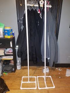 two coats are hanging on the clothes rack in front of a black door with white piping