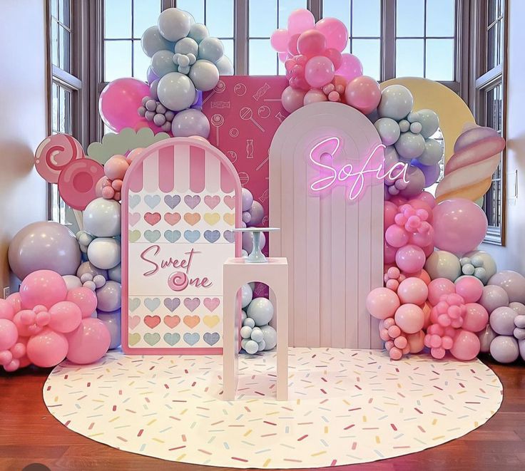 a room with balloons and decorations on the wall, including a sign that says sweet one