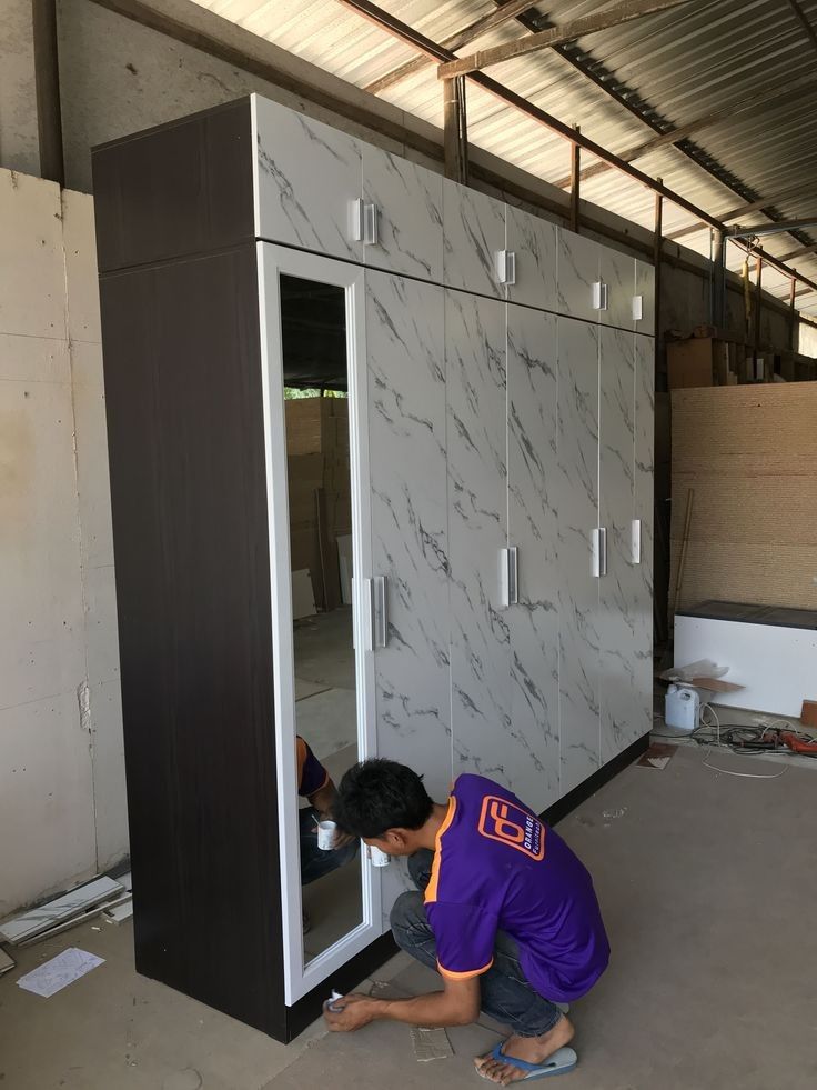 a man kneeling down next to a tall cabinet