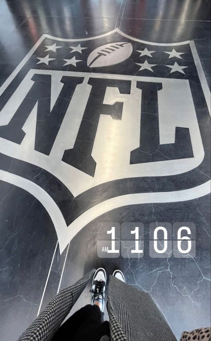 the feet of a person standing in front of a nfl logo on a floor that is painted black and white