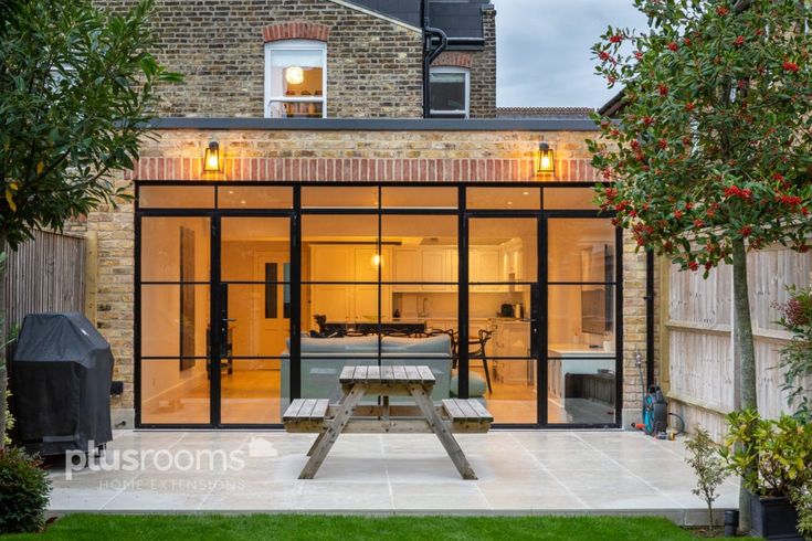 an outdoor dining area with glass walls and sliding doors leading to the back patio, surrounded by greenery