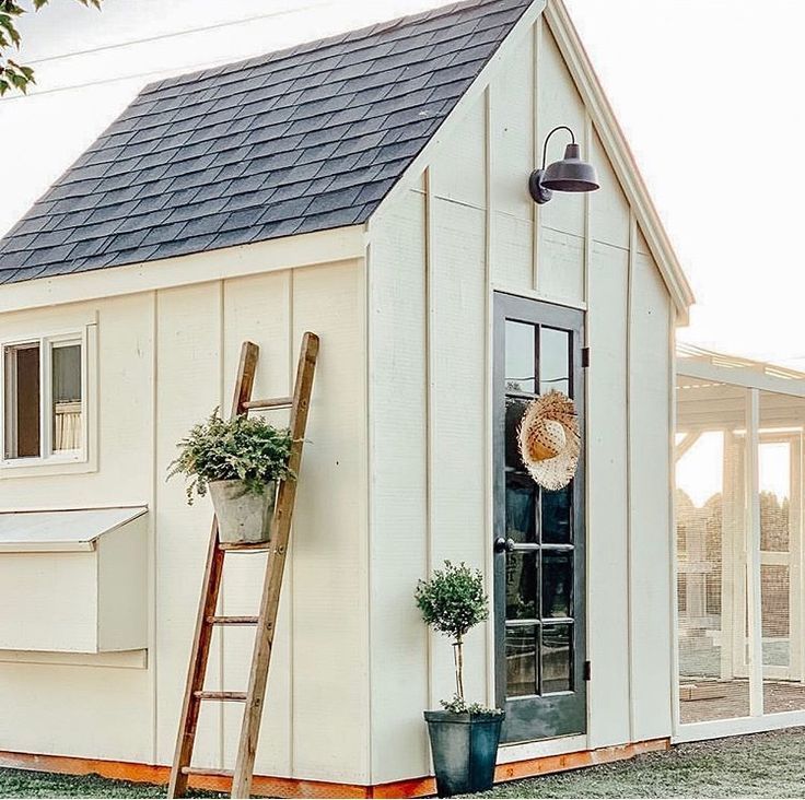 a ladder leaning against the side of a white shed with a potted plant on it