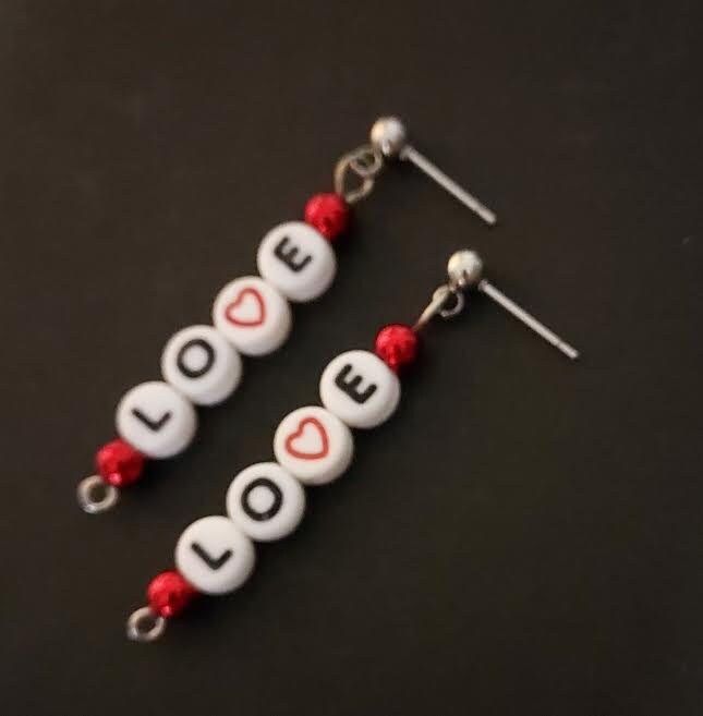 two pairs of earrings with the word love spelled out in white letters and red beads