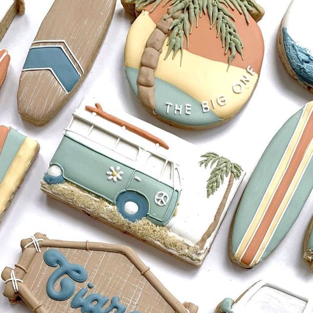 decorated cookies with surfboards and cars are on a white tablecloth that says the big one