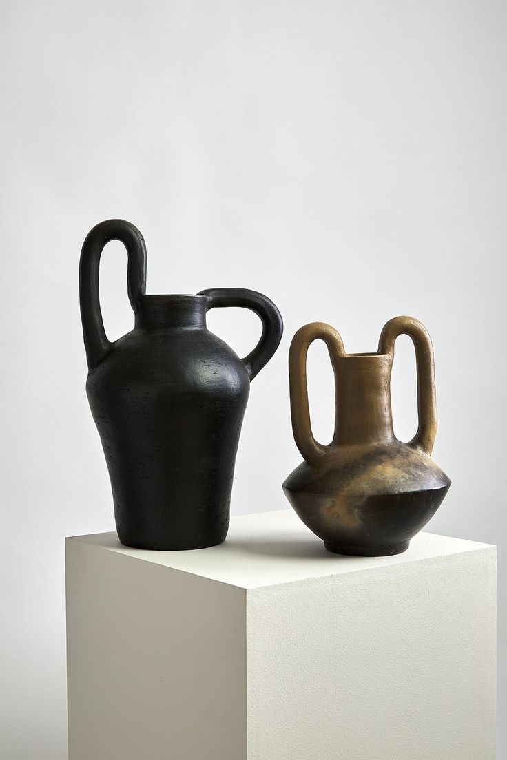 two black and brown vases sitting on top of a white block