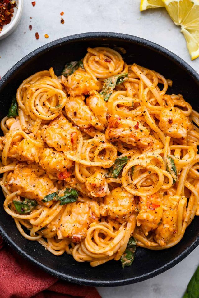 pasta with chicken and spinach in a skillet next to lemon wedges on the side