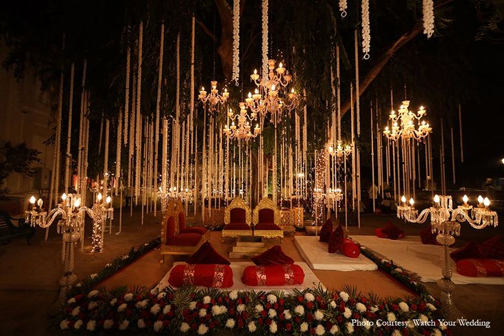 an outdoor wedding setup with chandeliers, candles and flower arrangements on the ground