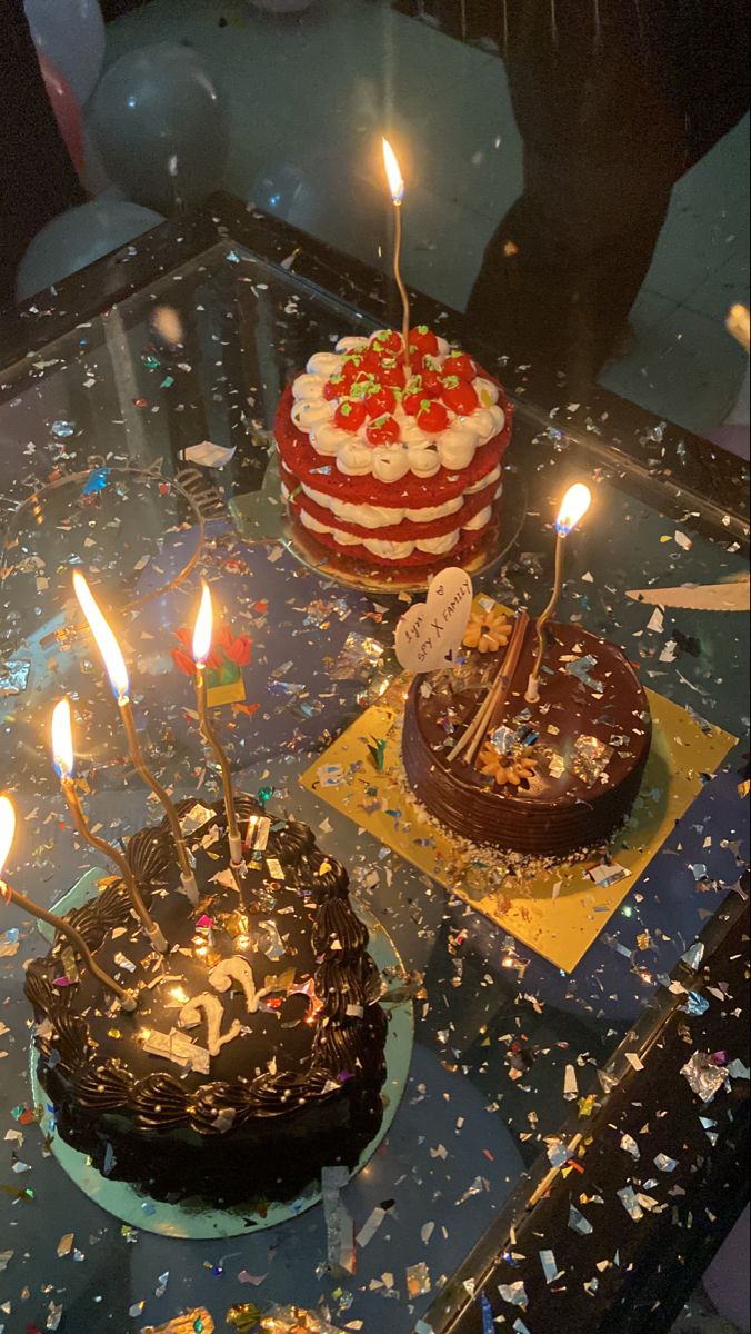 two cakes with lit candles on them sitting on top of a glass table covered in confetti and sprinkles