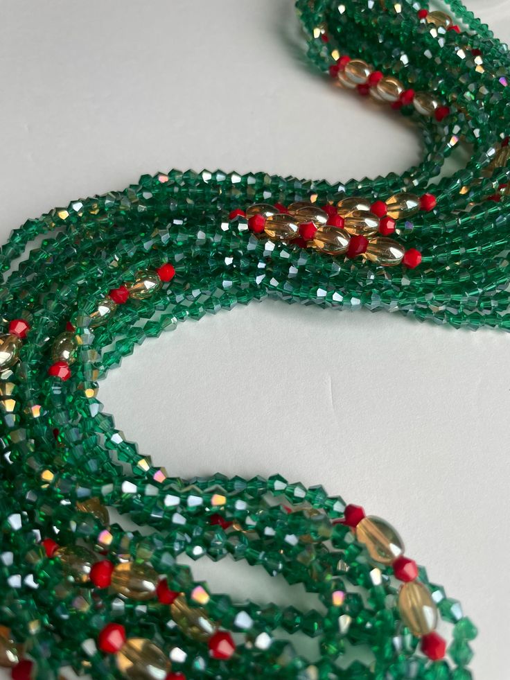 Elastic waist beads, made by skilled artisans in the Ivory Coast. This striking piece features deep green crystal glass seed beads complemented by vibrant red crystal glass seed bead accents, blending nature's tranquility with bold energy. Cultural Significance: In the Ivory Coast, waist beads hold deep cultural meaning as symbols of femininity, sensuality, and personal growth. Traditionally worn to celebrate significant life events, these beads connect wearers to their heritage and empower their personal journeys. Design and Craftsmanship: Materials: High-quality crystal glass seed beads Colors: Deep Green: Represents growth, harmony, and renewal Red Accents: Symbolizes passion, vitality, and strength Fit: Elastic band ensures a comfortable and flexible fit for all body types Wear with Pu Green Multi-strand Beads For Gifts, Green Round Beads Spiritual Crystal Necklace, Traditional Green Faceted Beaded Necklaces, Bohemian Green Waist Beads With Colorful Beads, Traditional Green Faceted Beaded Necklace, Multi-strand Green Faceted Beads, Green Multi-strand Beaded Bracelets With Faceted Beads, Green Gemstone Party Beads, Bohemian Green Waist Beads