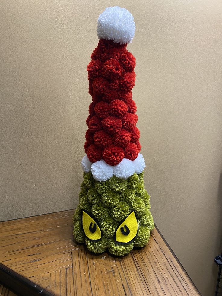 a knitted christmas hat sitting on top of a green and red thing with yellow eyes