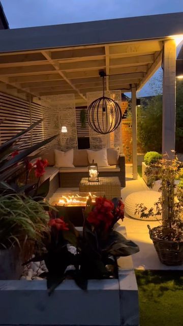 an outdoor living area is lit up at night with lights on and flowers in the foreground