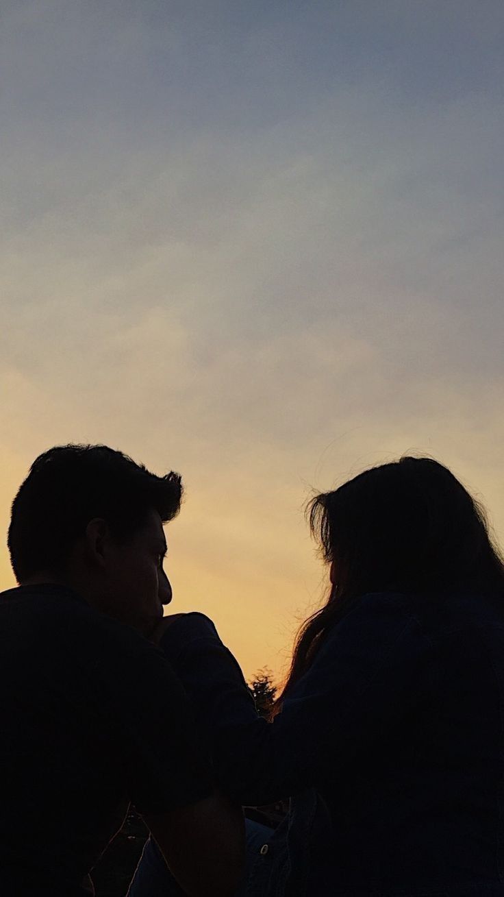 two people are flying a kite in the sky at sunset or dawn with one person watching