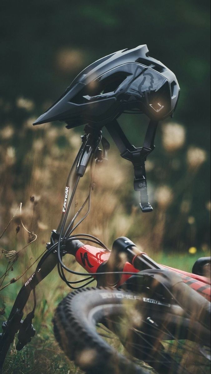 a close up of a bicycle helmet on the ground with grass in the background and weeds growing all around