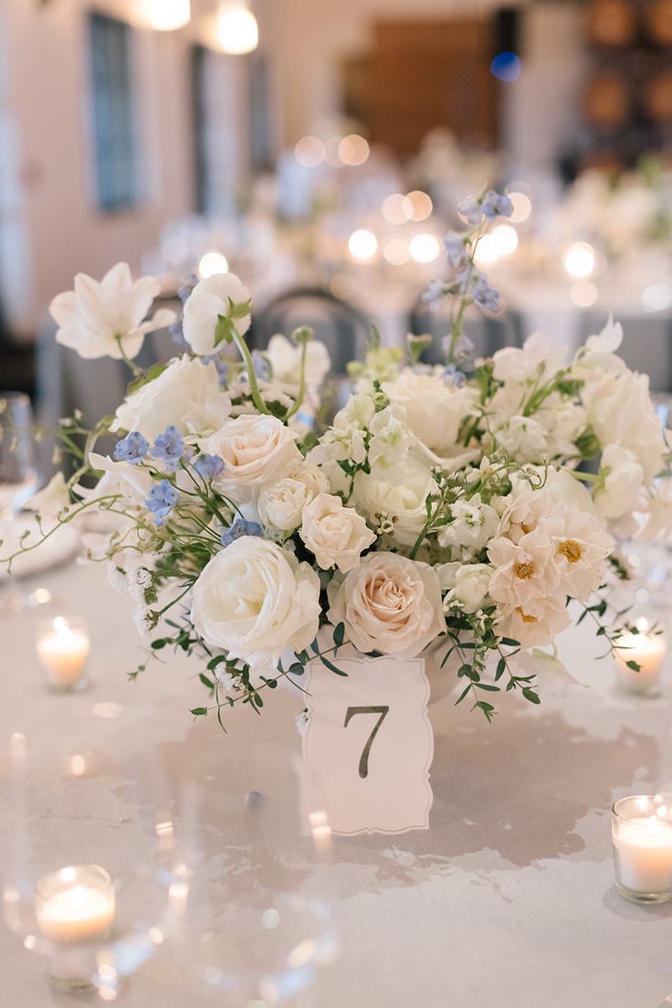 a vase filled with white and blue flowers on top of a table next to candles