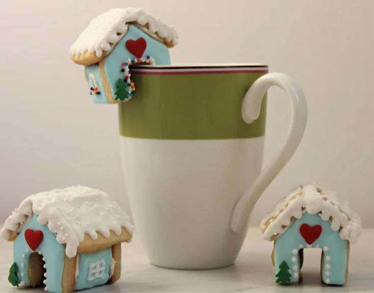 there is a cup and some cookies in the shape of houses next to each other