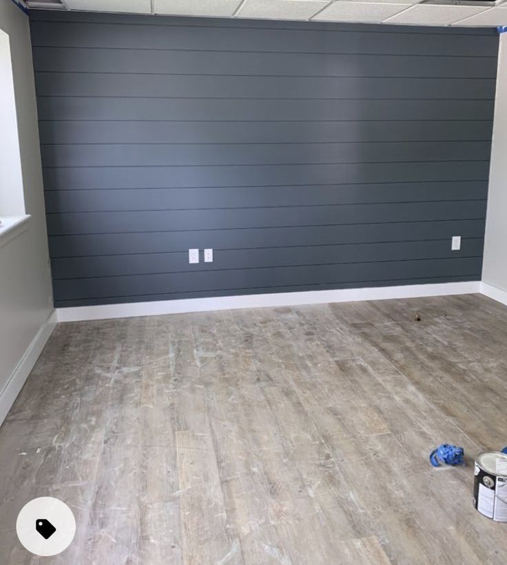 an empty room with hard wood flooring and gray painted walls in the background, there is a paint roller on the floor