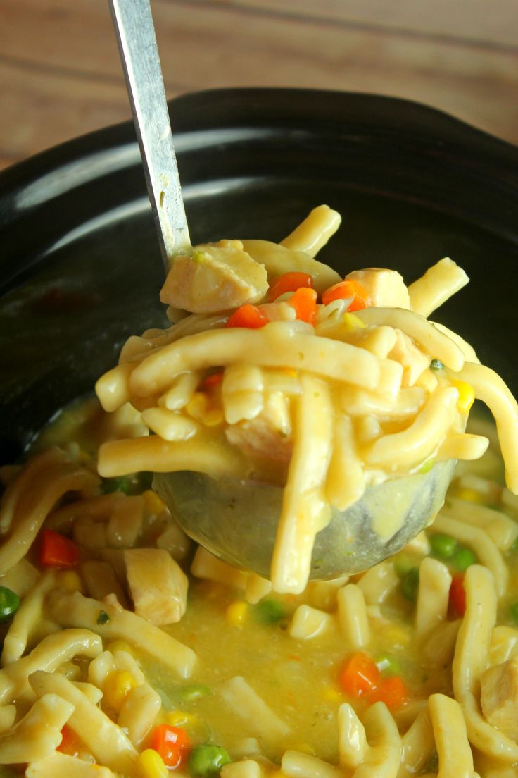 a ladle full of noodles and vegetables being held by a spoon