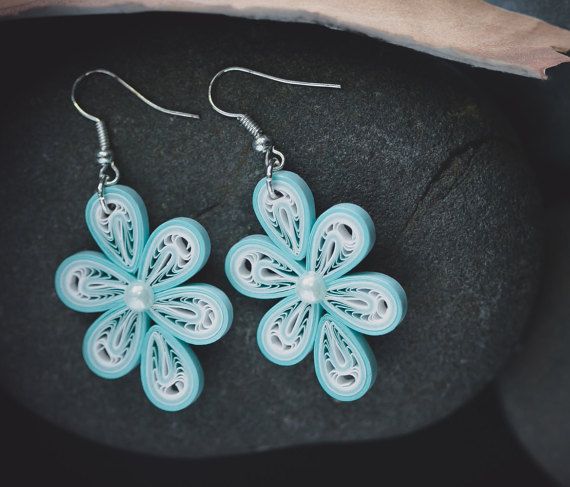 a pair of blue earrings sitting on top of a black stone covered ground next to a piece of paper