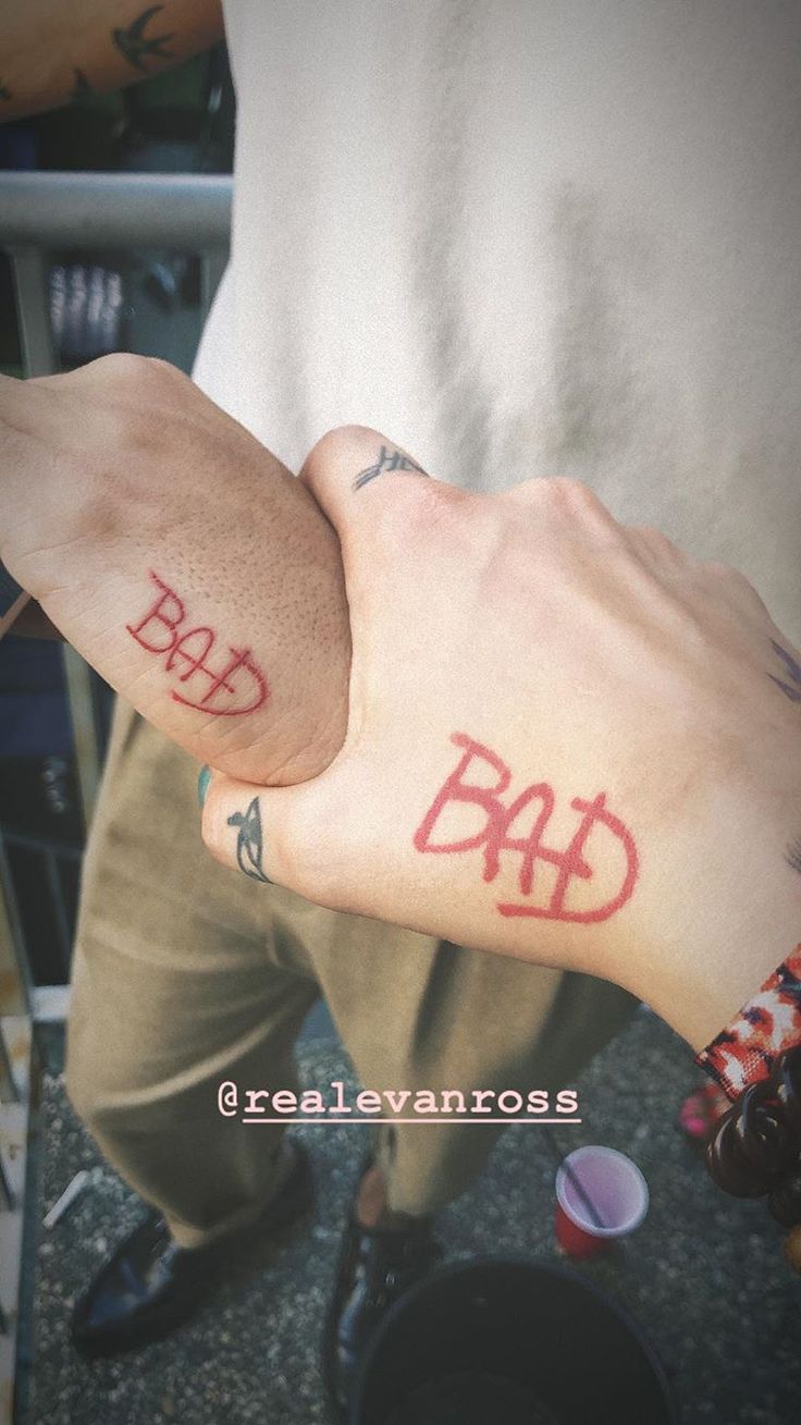 two people with tattoos on their arms holding each other's hands and one has the word bad written on it