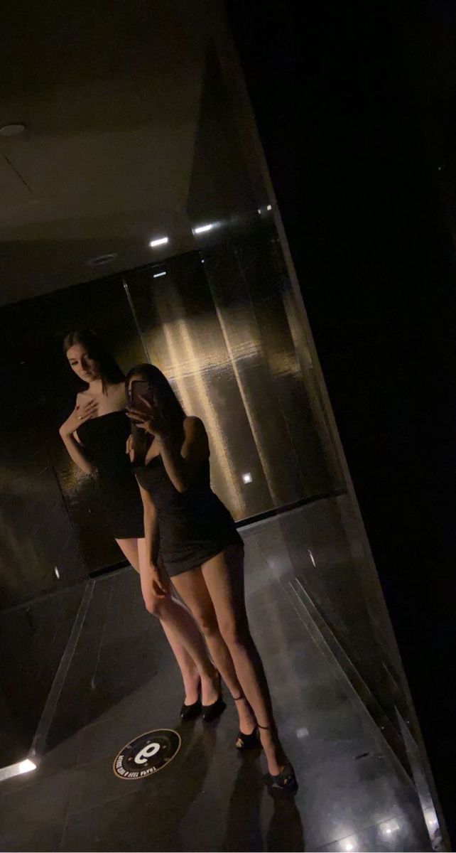 two women standing in front of a mirror with their backs turned to the opposite direction