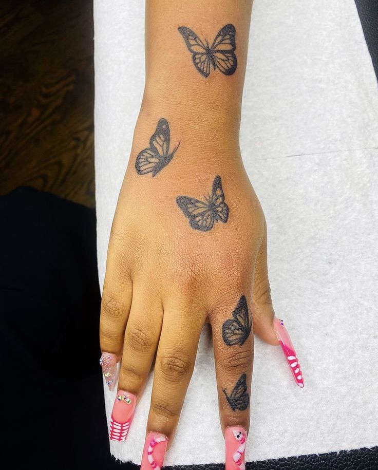 a woman's hand with butterfly tattoos on her left arm and pink nail polish