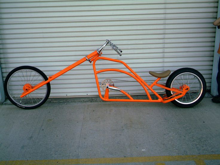 an orange bike is parked in front of a garage door with a man standing next to it