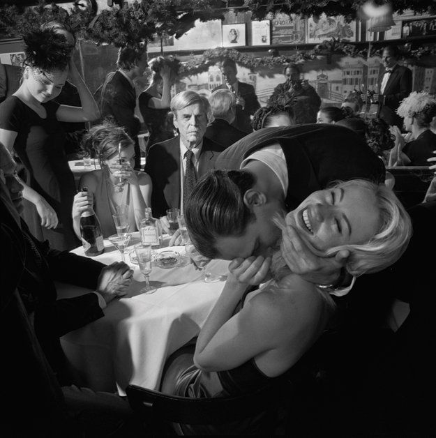 a black and white photo of a woman hugging another woman's face at a dinner table