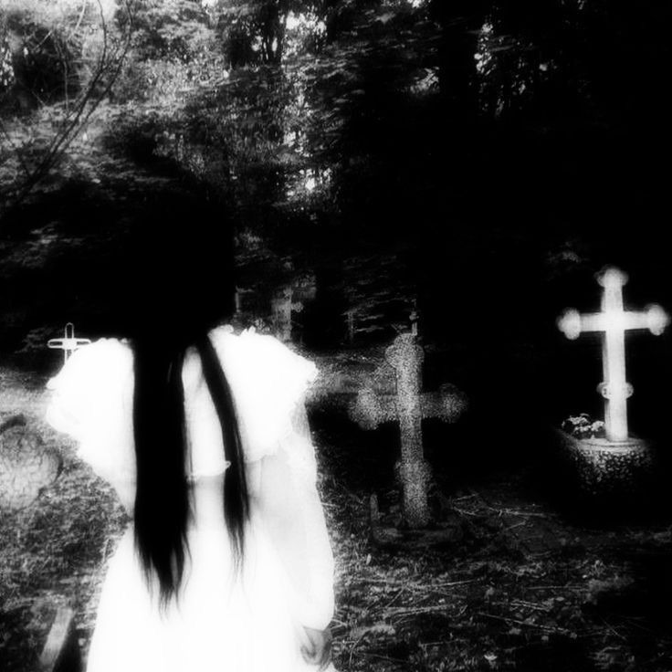 a woman with long hair standing in front of a cross on a cemetery path,