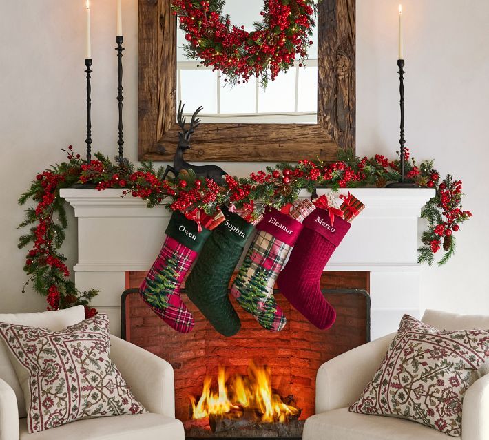 christmas stockings hung over the fireplace in front of a wreath and fire place with candles