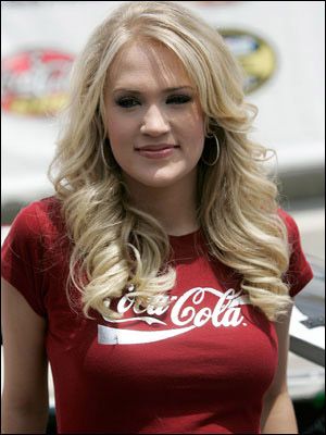 a woman with long blonde hair wearing a coca cola t - shirt and looking at the camera