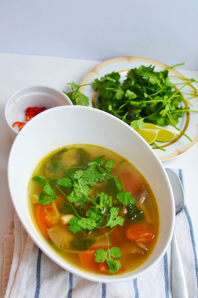 a bowl of soup with cilantro, carrots and parsley on the side