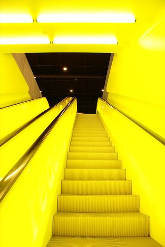 an escalator with yellow steps leading up to the ceiling and lights above it