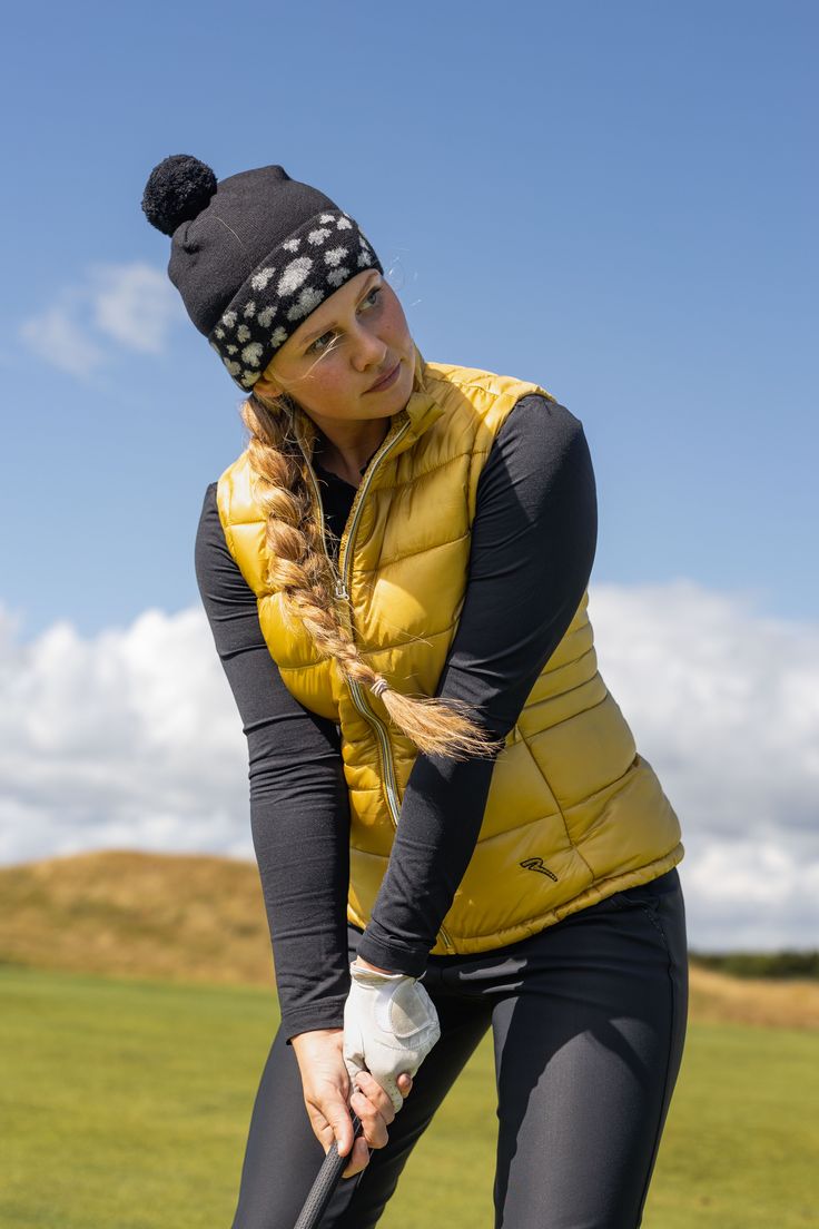 a woman holding a golf club on top of a green field