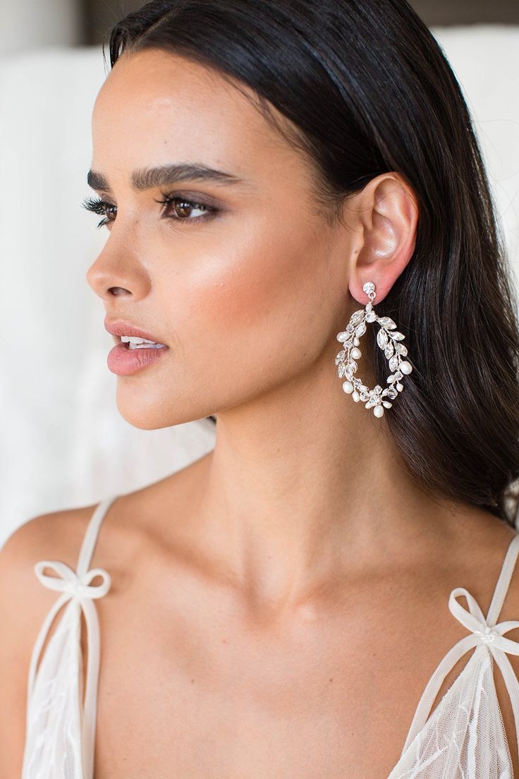 a woman in a white dress is wearing large earrings with bows on the sides and pearls hanging from them