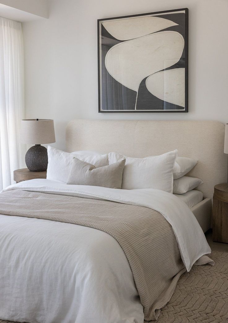 a bed with white sheets and pillows next to a painting on the wall above it