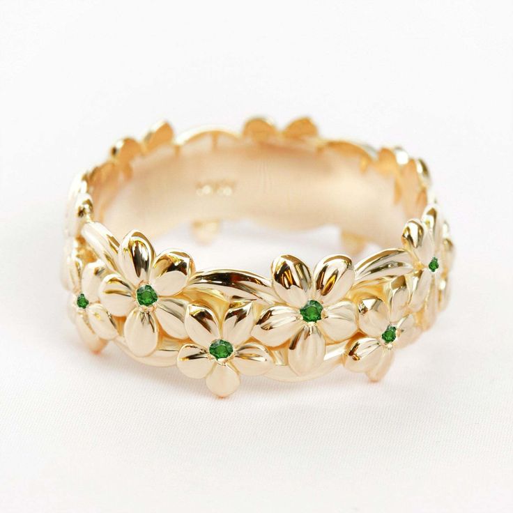 a gold ring with flowers and green stones on the inside, sitting on a white surface