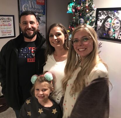 a group of people standing next to each other in front of a christmas tree with pictures on the wall