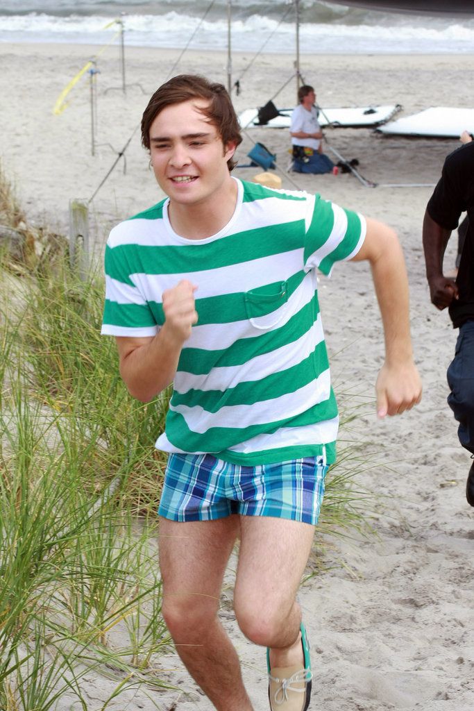 a young man running on the beach in shorts and a green striped t - shirt