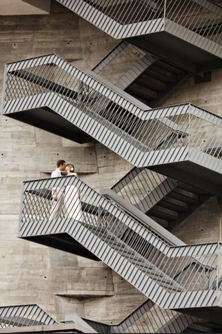 two people walking up and down the side of a building with metal balconies